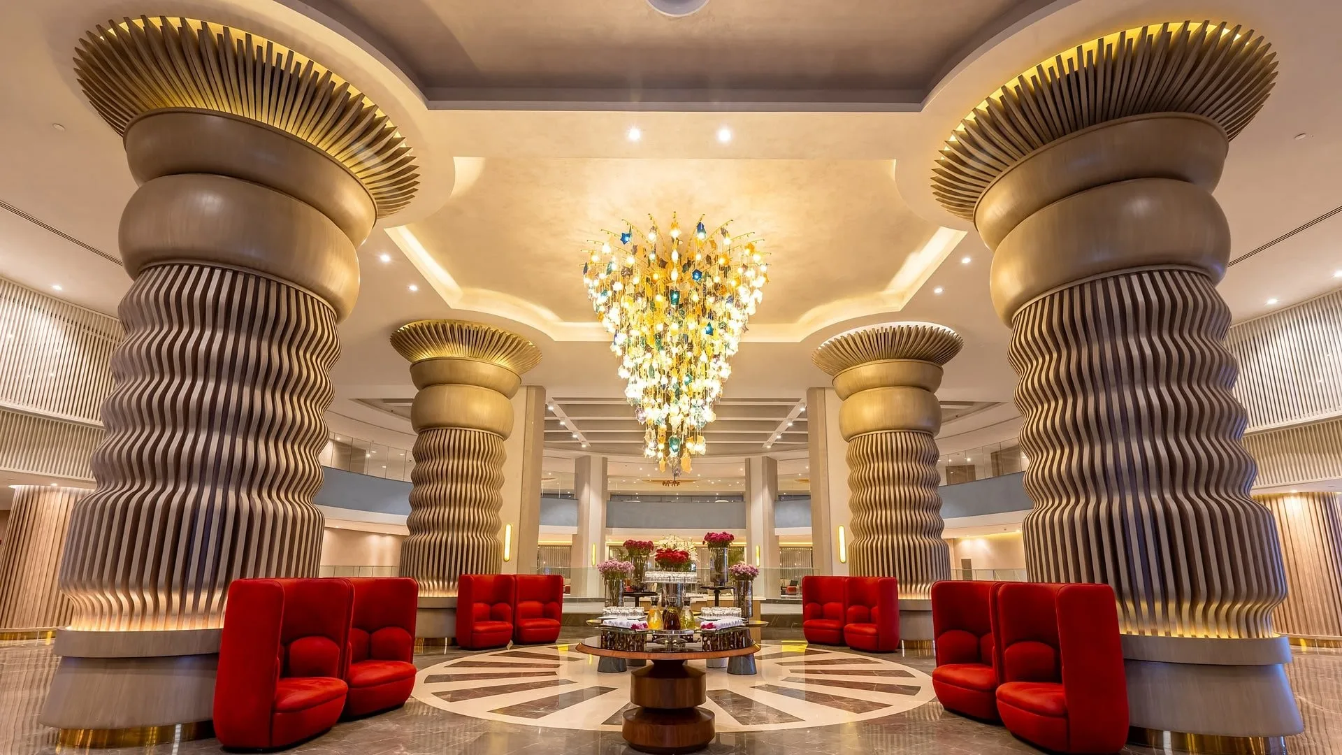 Lobby elegante con imponenti colonne decorate, lampadario e poltrone rosse