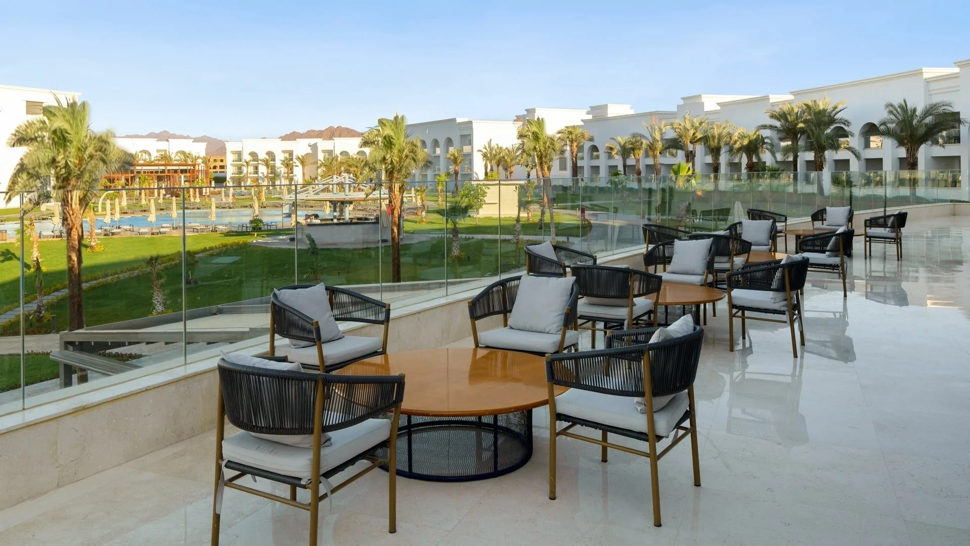 Terrazza con poltrone e tavoli affacciata sul giardino e piscina del resort