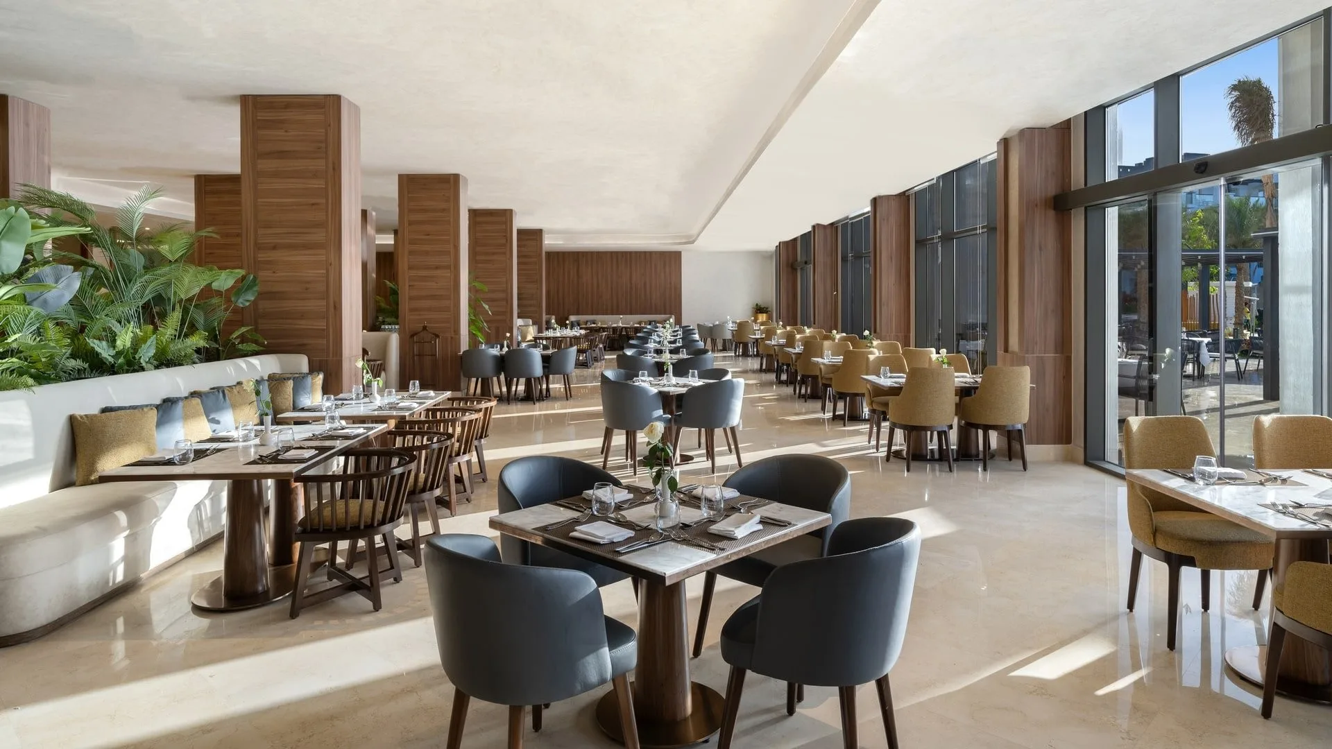 Sala ristorante moderna e luminosa con tavoli apparecchiati e piante verdi