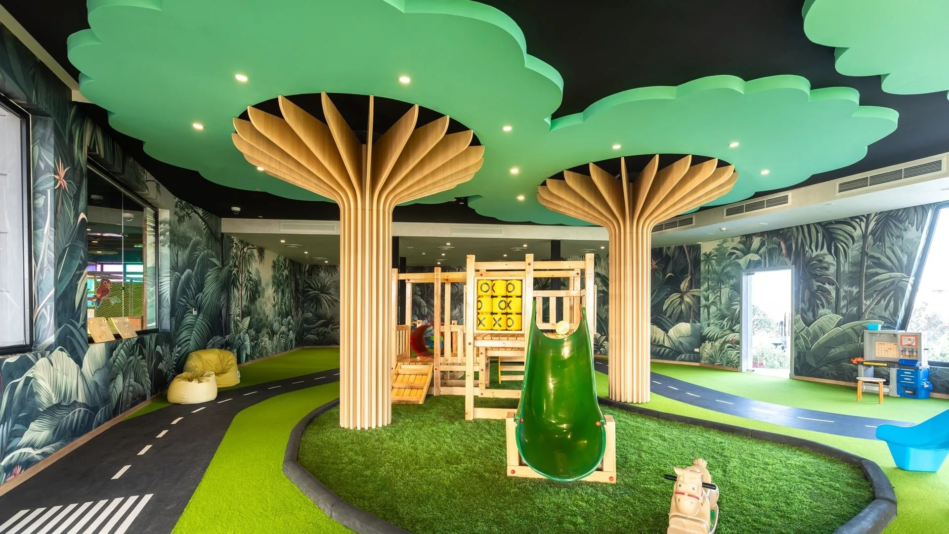 Area giochi interna per bambini a tema giungla con scivolo e alberi stilizzati