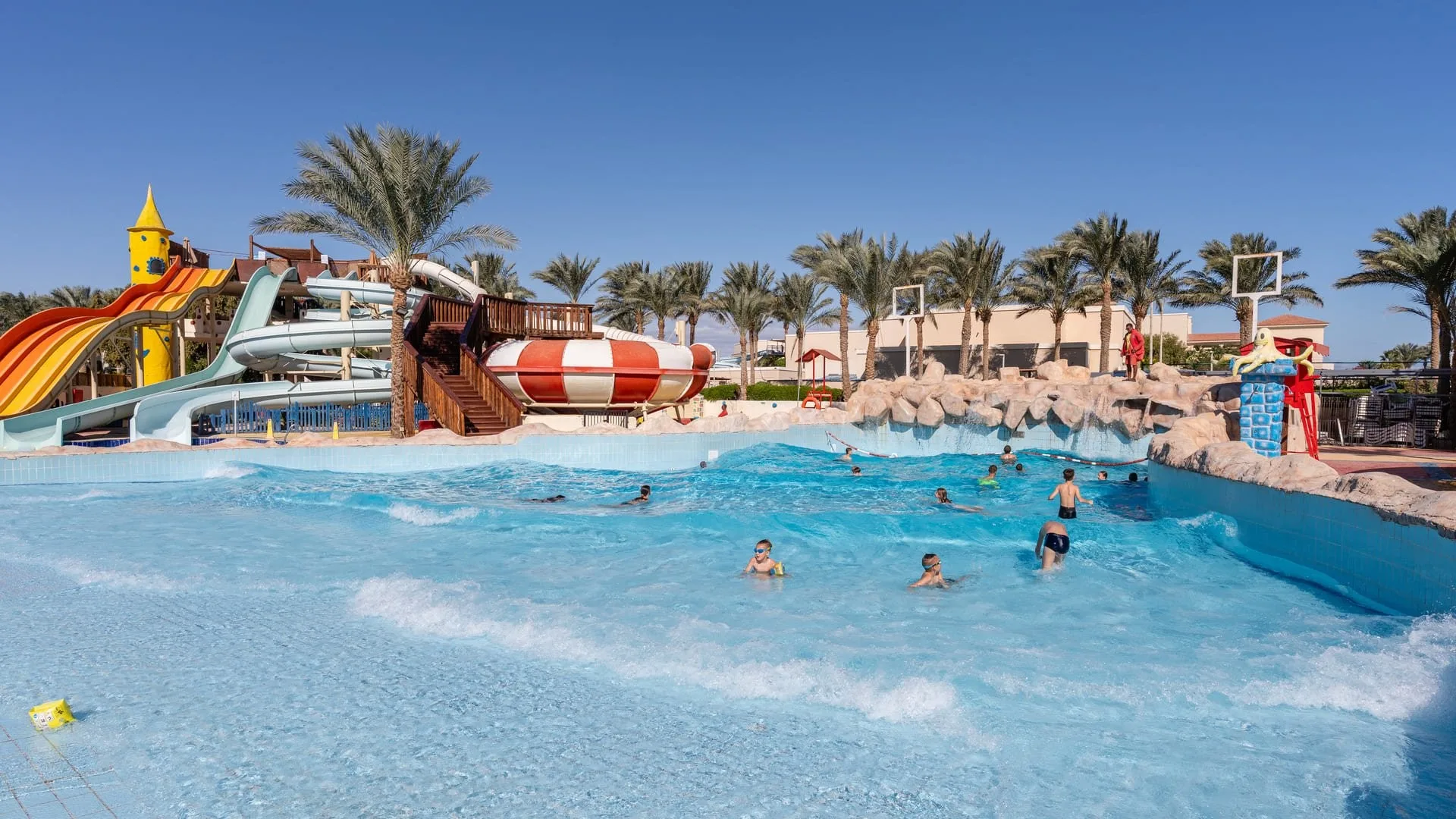 Piscina a onde con bagnanti e scivoli colorati circondati da palme