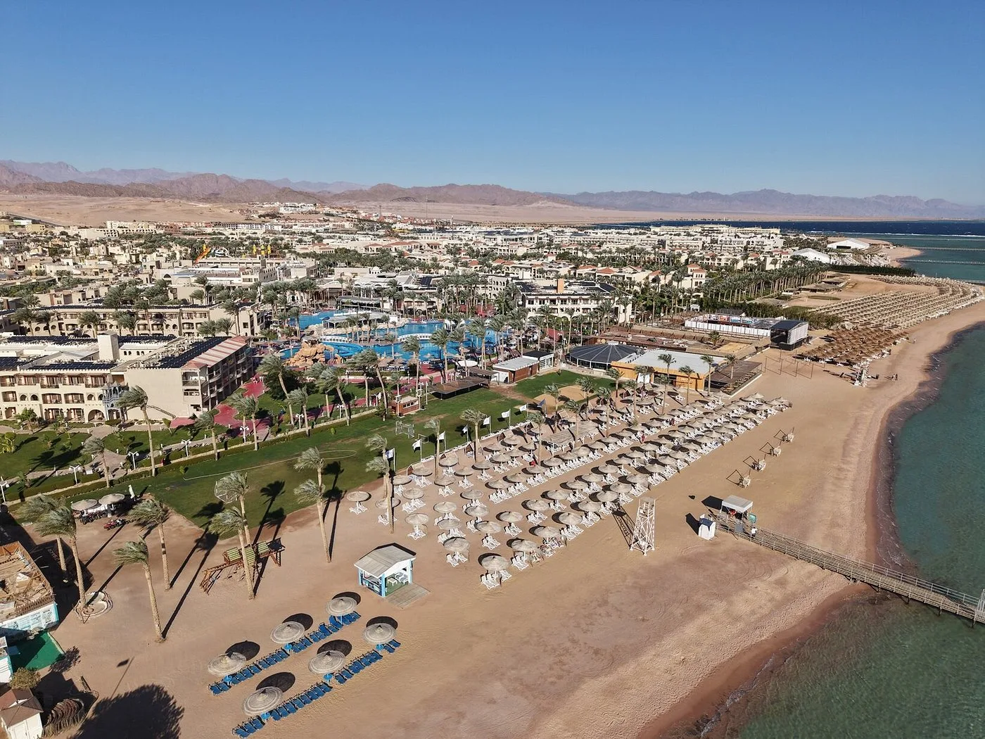 Veduta aerea della spiaggia del resort con ombrelloni, pontile e mare cristallino