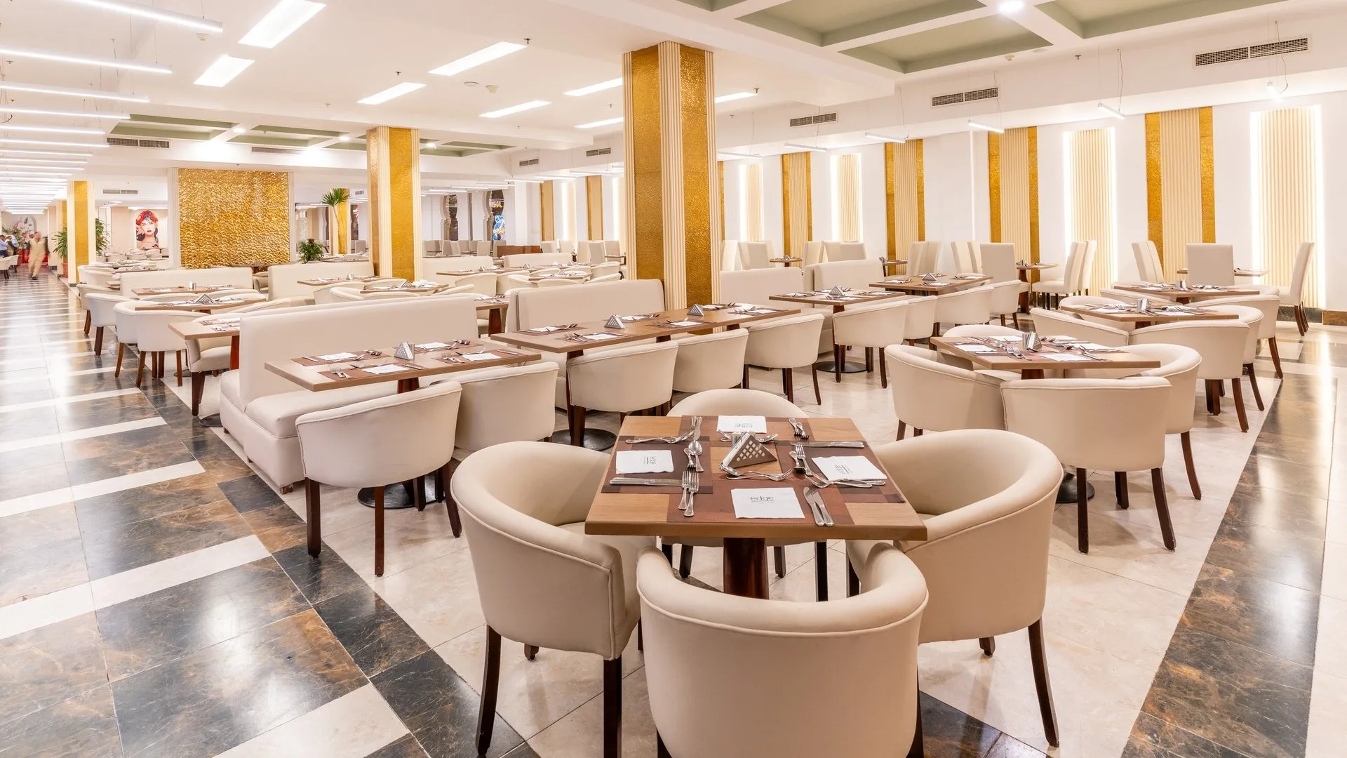 Ampia sala ristorante con tavoli apparecchiati, sedie beige e colonne dorate