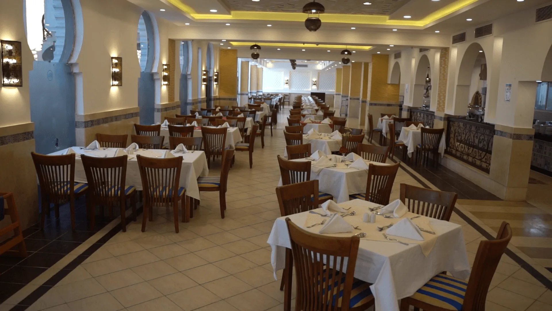 Sala ristorante in stile arabo con archi azzurri, tavoli bianchi e sedie in legno