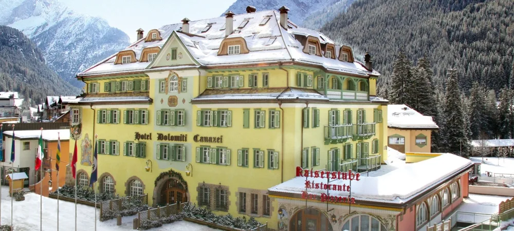 Esterno dell'Hotel Dolomiti Canazei con facciata storica gialla e montagne innevate