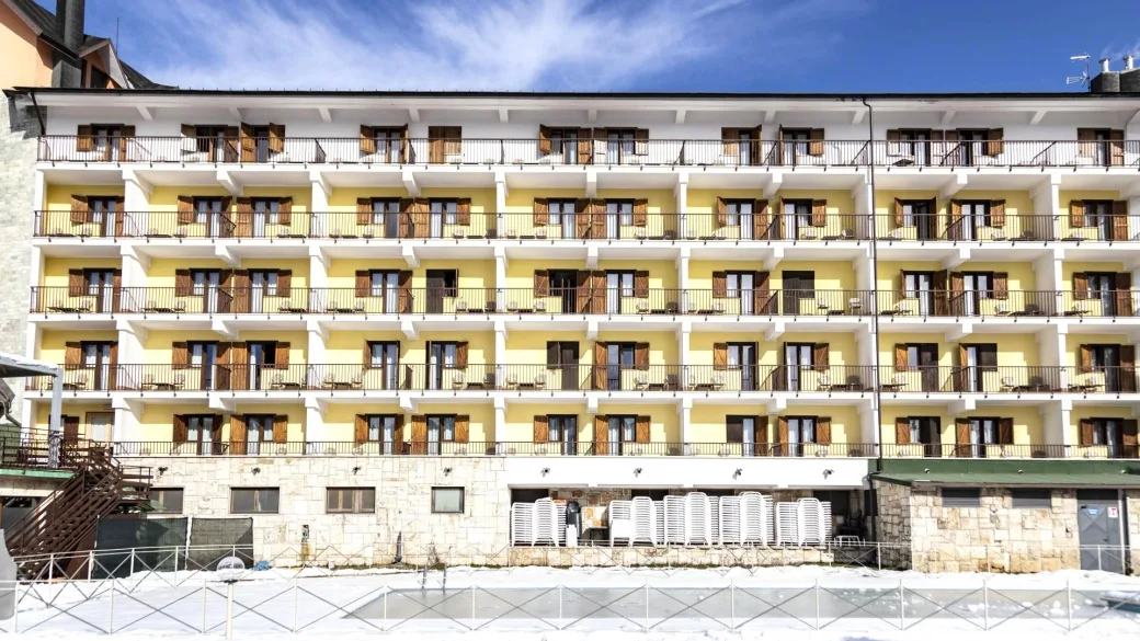 Facciata gialla dell'hotel con balconi e persiane in legno sotto un cielo azzurro