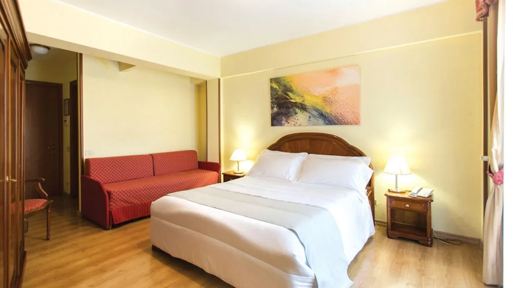 Camera dell'hotel con letto matrimoniale, divano rosso e pavimento in parquet