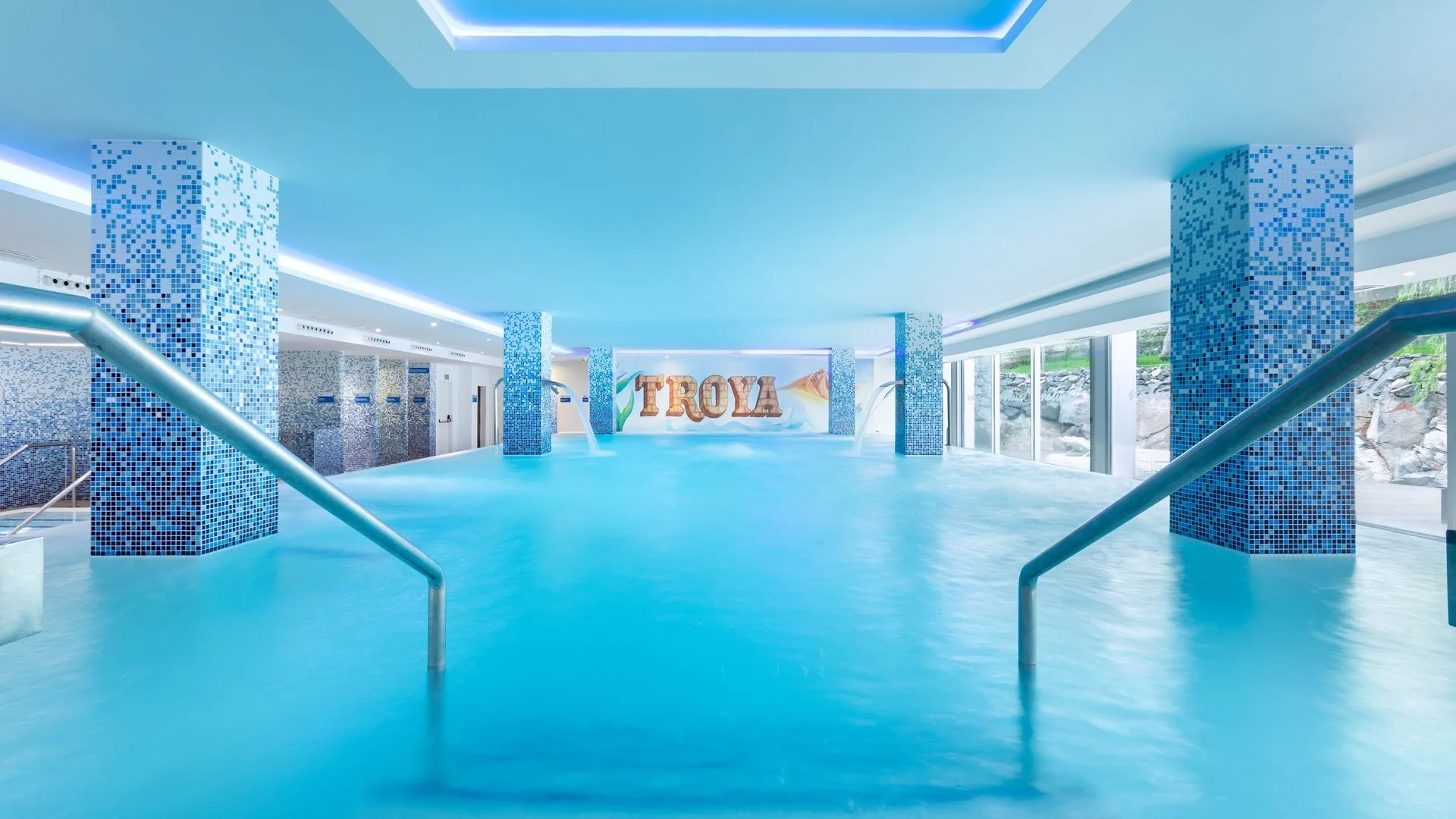 Piscina coperta termale con colonne a mosaico e scritta Troya sulla parete