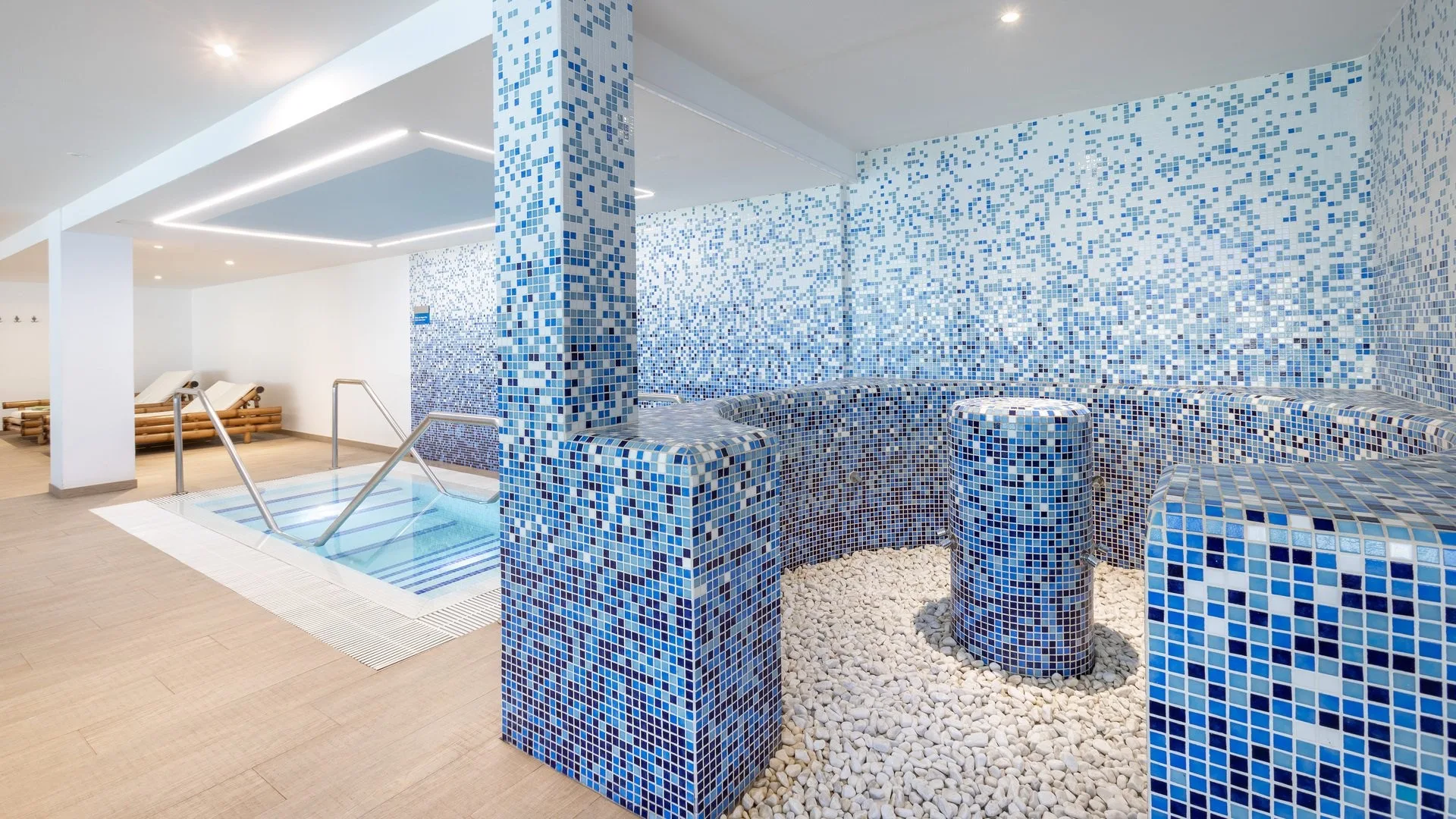 Zona spa con pareti a mosaico blu, vasca idromassaggio e dettagli in pietra bianca