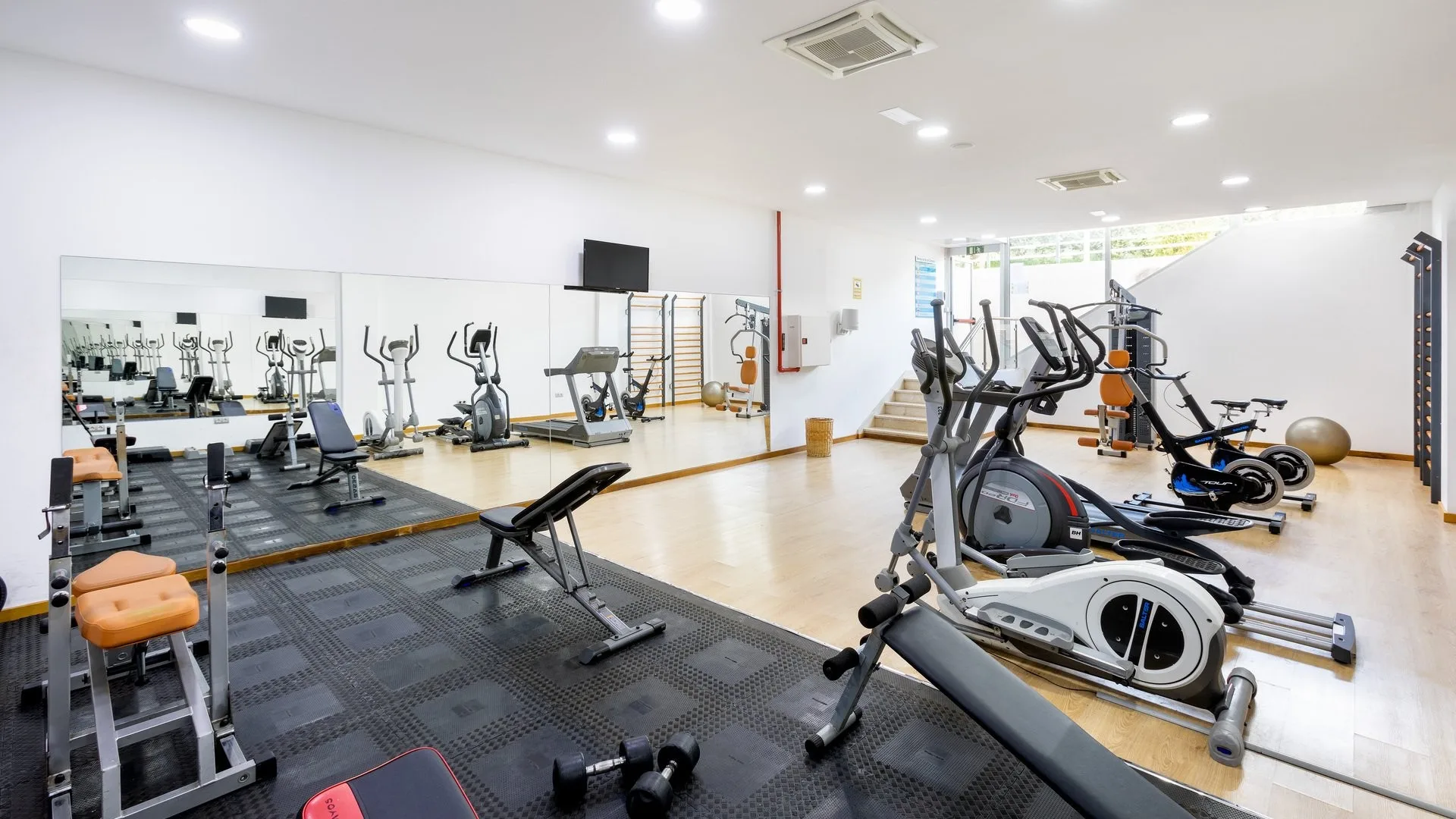 Palestra attrezzata con macchine cardio, pesi e grande specchio a parete