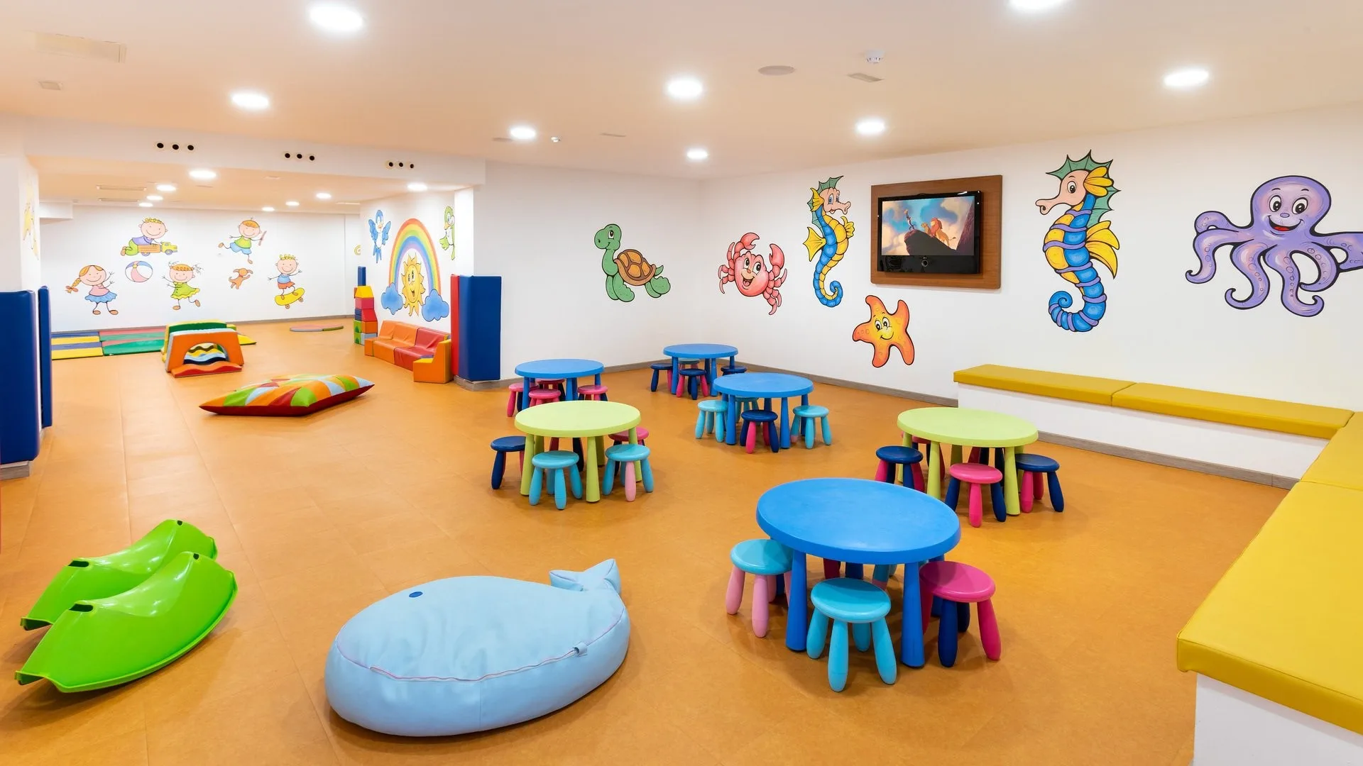 Area ludica per bambini con tavolini colorati, giochi morbidi e decorazioni marine