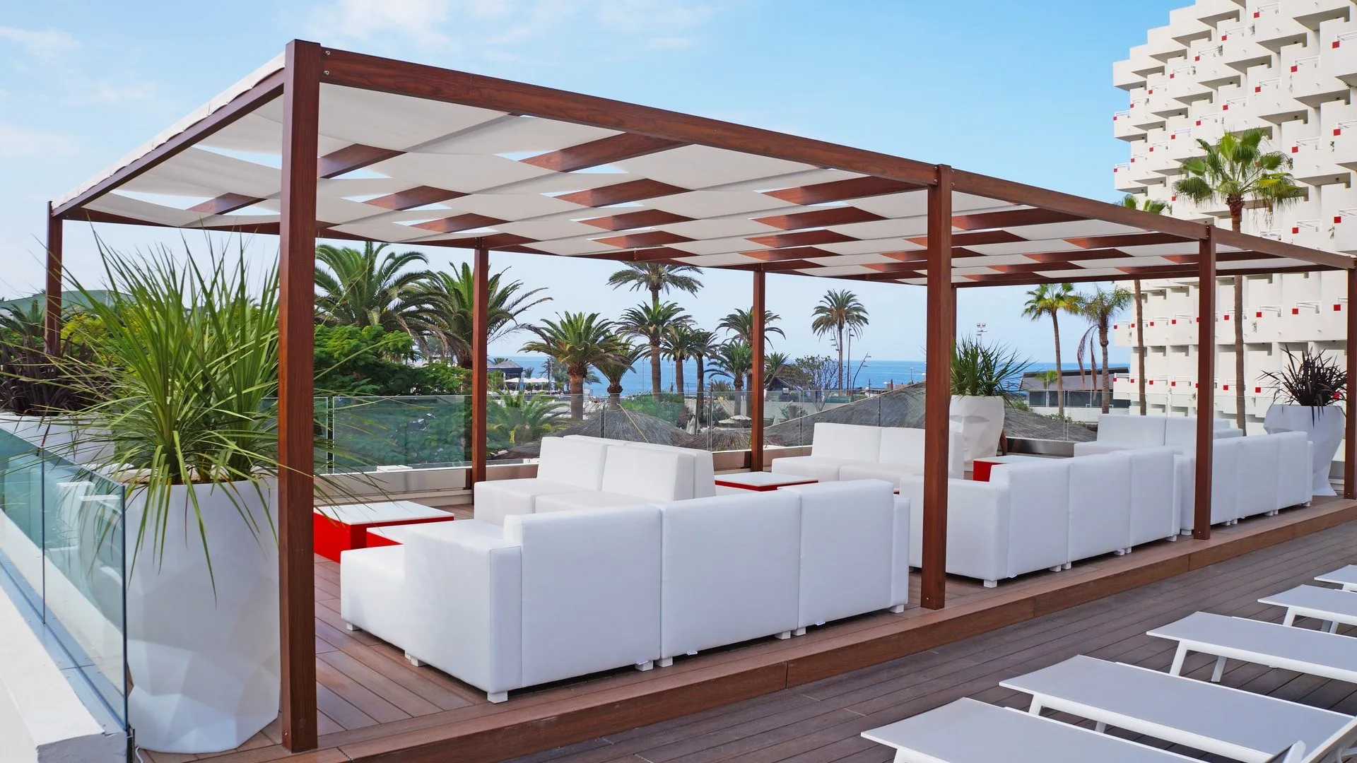 Terrazza con pergola in legno, divani bianchi e vista mare tra le palme