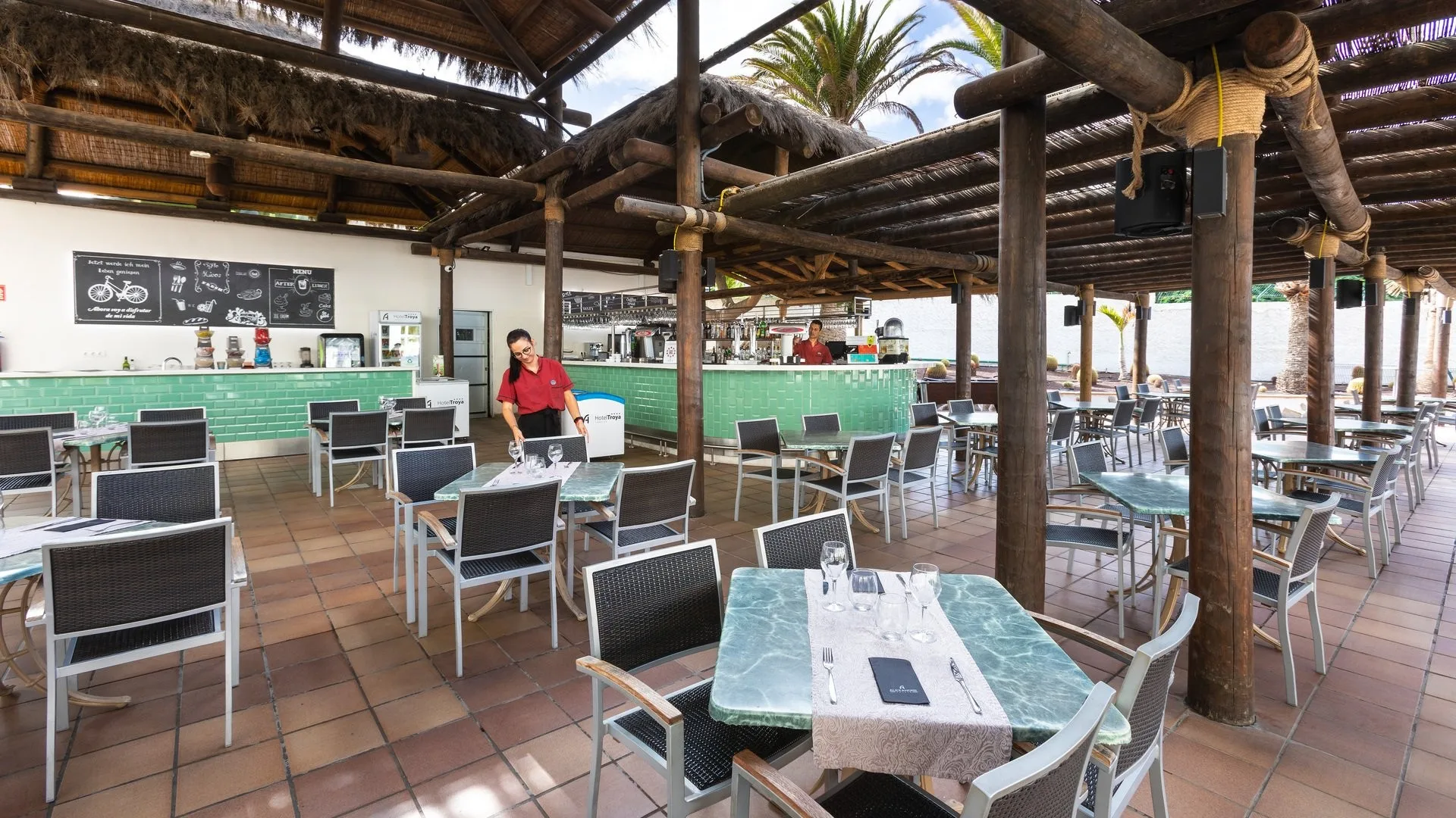 Bar ristorante all'aperto con copertura in legno, tavoli e vista sulla spiaggia