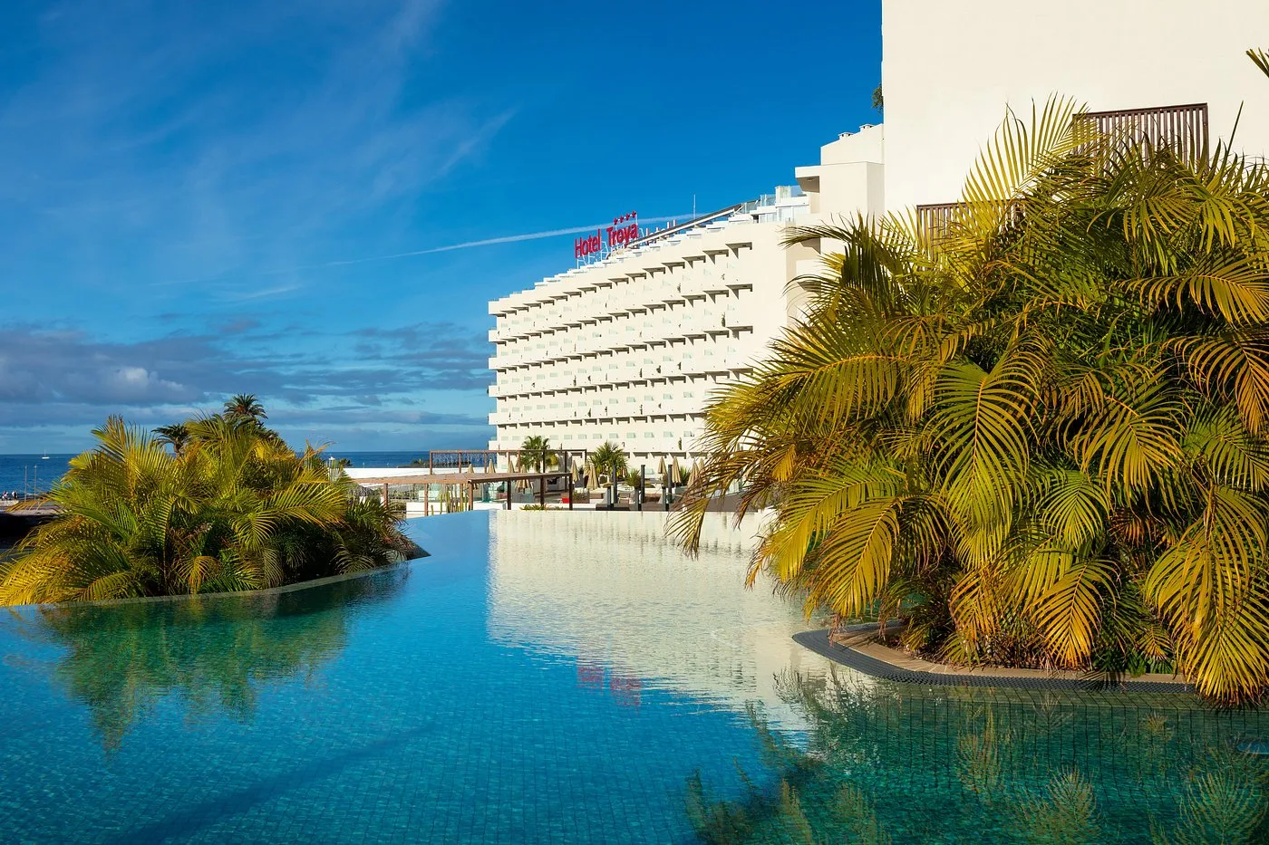 Vista dell'Hotel Troya dal giardino con piscina a sfioro e palme riflesse nell'acqua