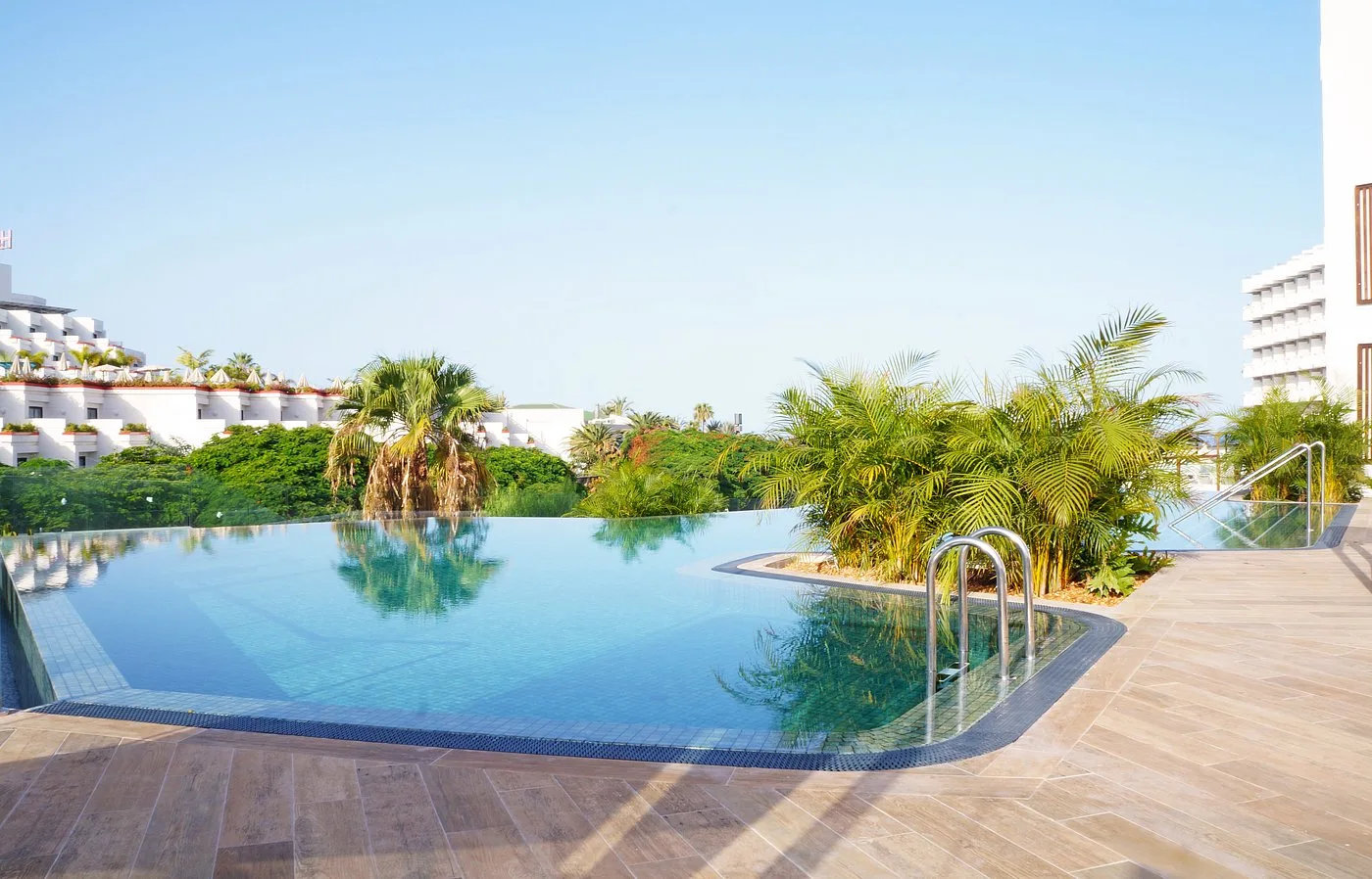 Piscina a sfioro con vegetazione tropicale e vista sugli edifici dell'hotel