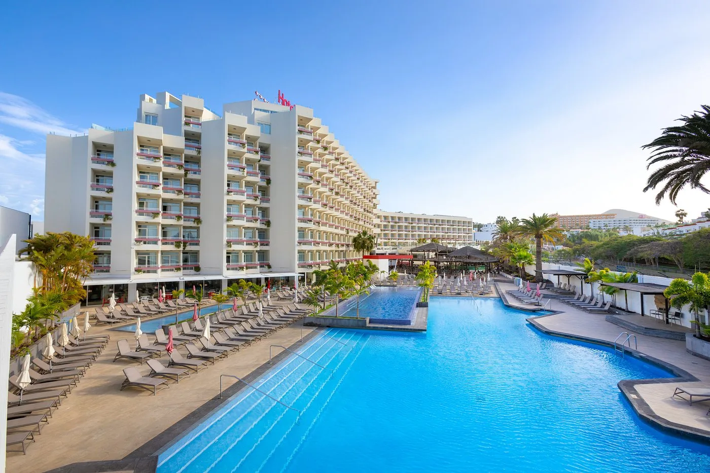 Veduta dell'hotel con ampia piscina, lettini allineati e giardino tropicale