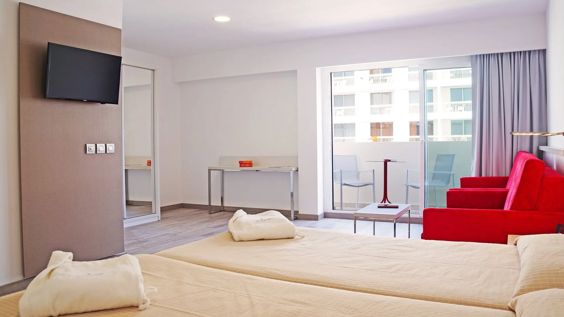 Camera moderna con letto, divano rosso, TV e accesso al balcone