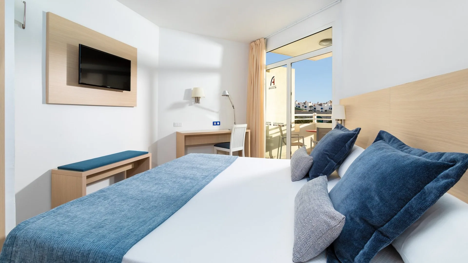 Camera con letto matrimoniale, cuscini blu, TV e balcone
