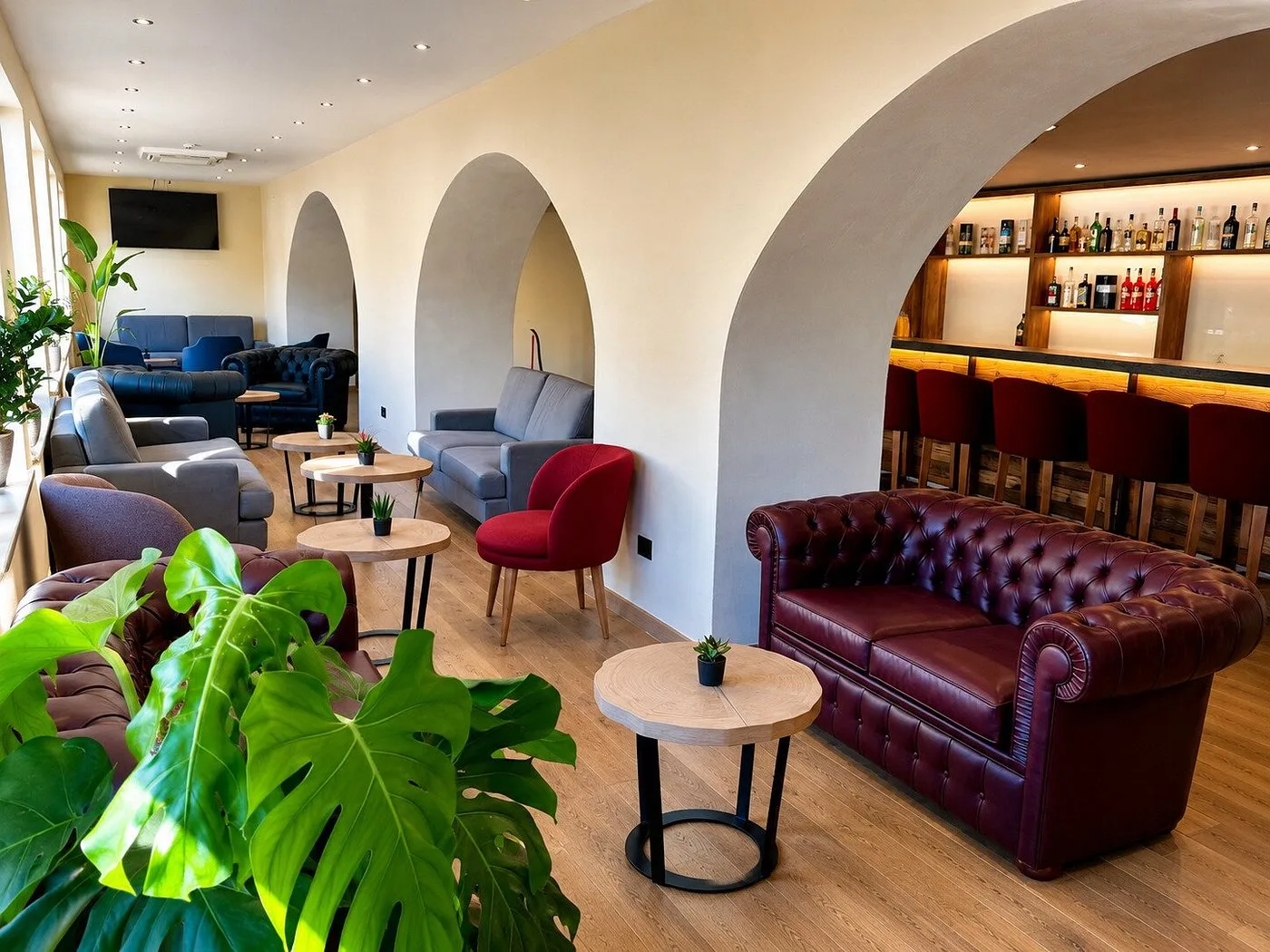 Lounge bar con divani in pelle bordeaux, archi bianchi e bancone con bottiglie