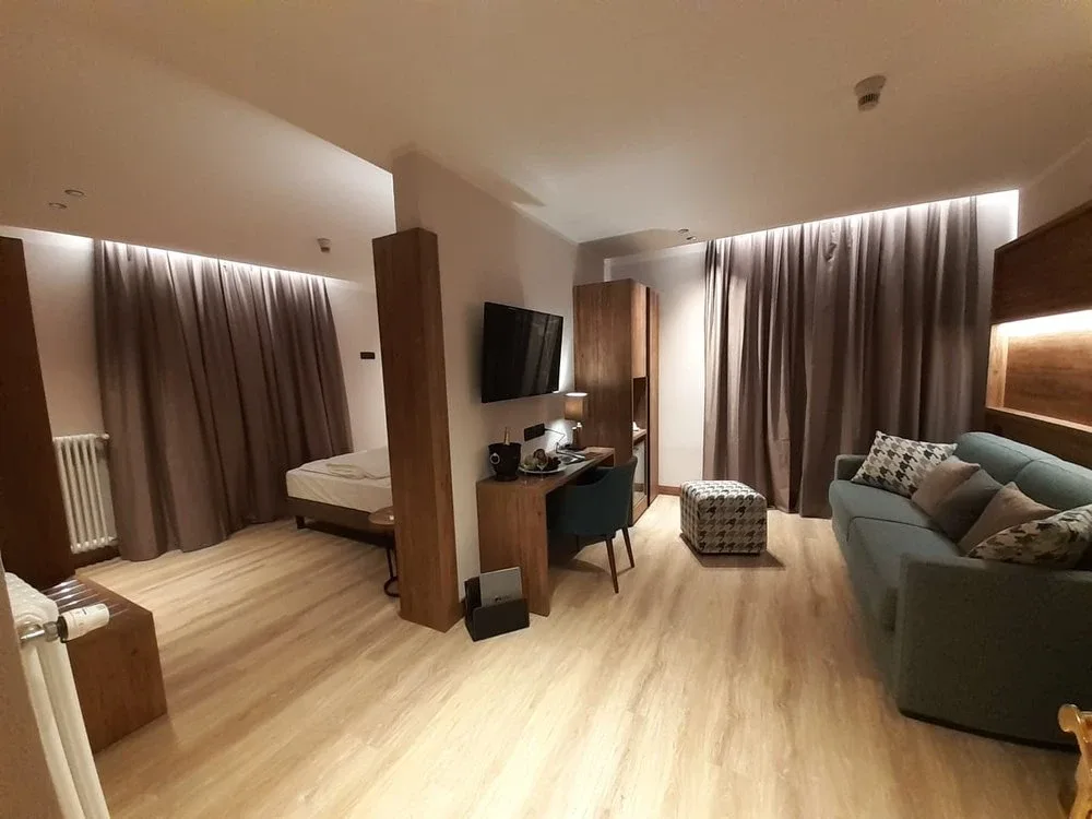 Ampia camera con zona notte, scrivania, TV e divano in tonalità calde