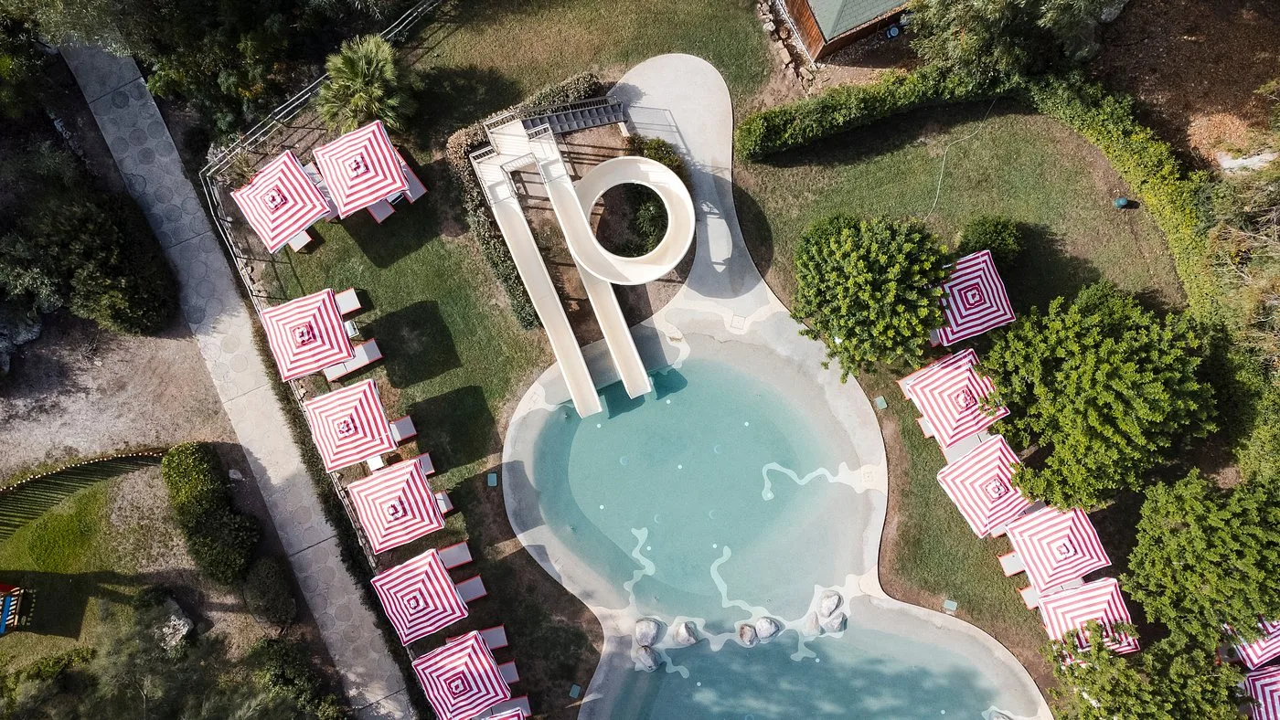 Vista aerea di piscina per bambini con scivolo e ombrelloni rossi a righe