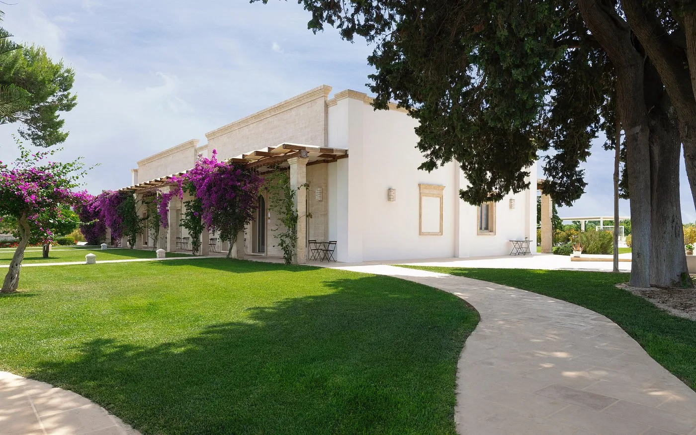 Vialetto tra prati verdi con bougainvillea fiorita lungo la facciata della masseria