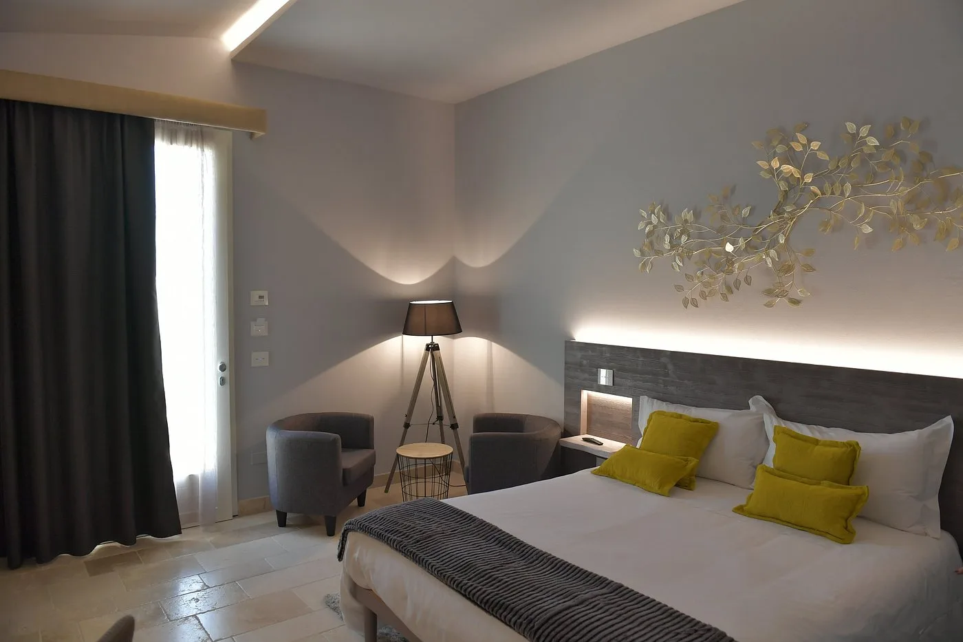 Camera elegante con letto, cuscini gialli, poltrone grigie e decoro a parete