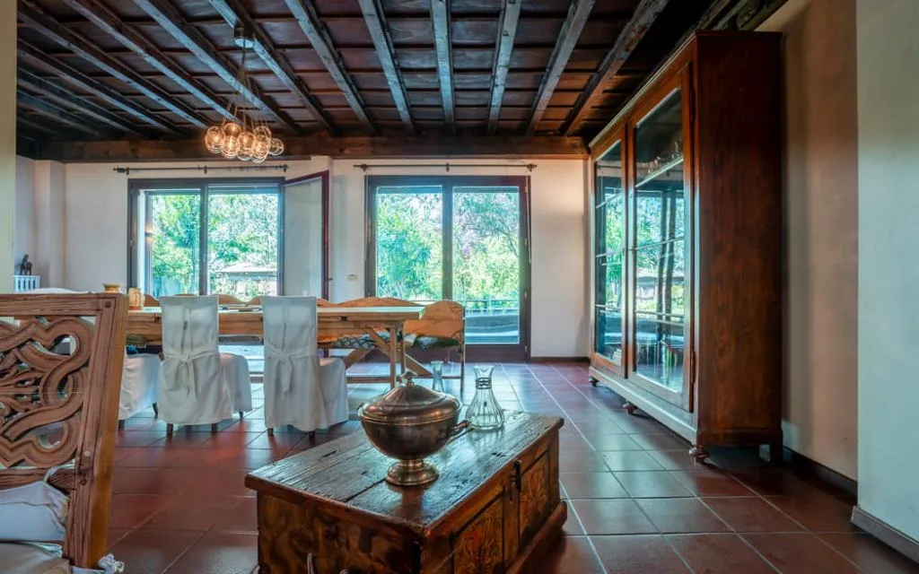 Sala da pranzo rustica con soffitto in legno, tavoli in legno e vista sul giardino