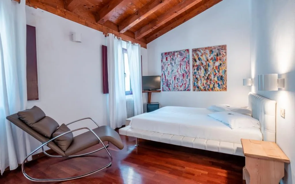 Camera mansardata con soffitto in legno, chaise longue in pelle e dipinti colorati