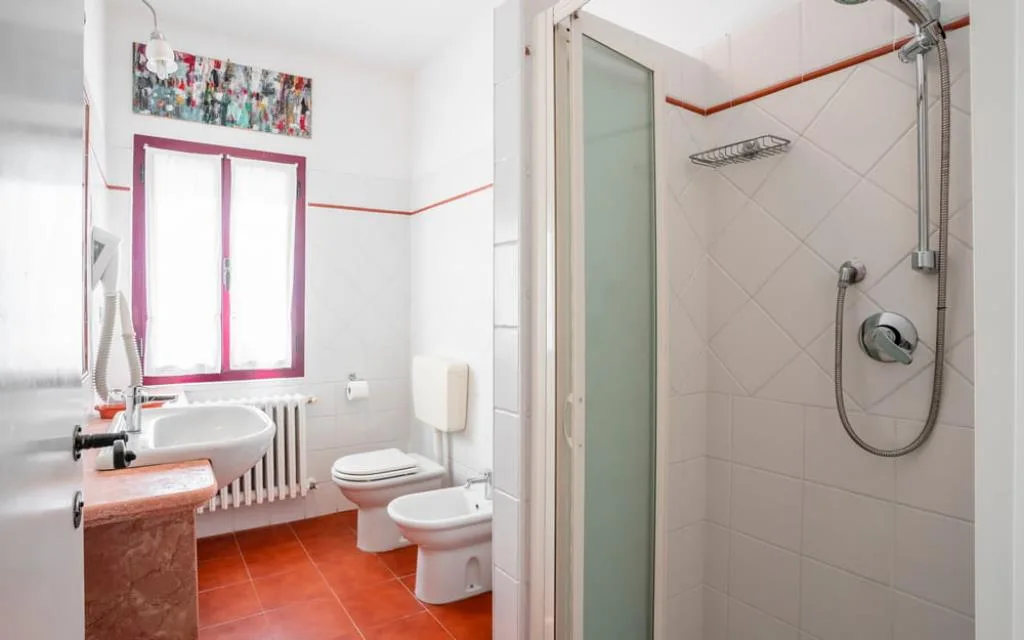 Bagno con doccia, lavabo su mensola in marmo, bidet e finestra con cornice bordeaux