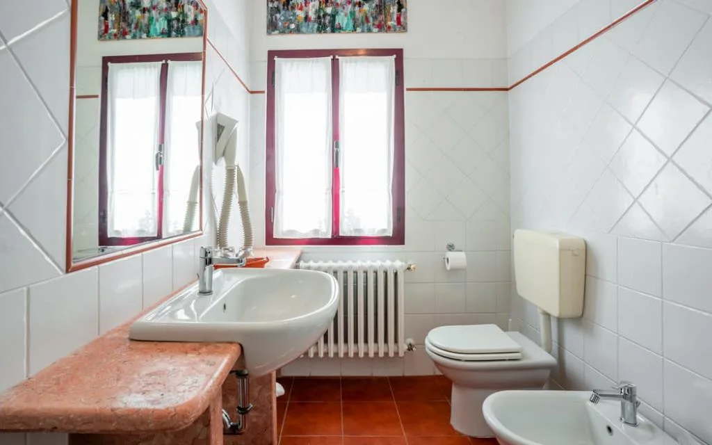 Bagno luminoso con lavabo su piano in marmo rosa, bidet e finestra doppia