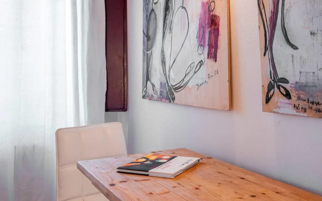 Dettaglio di scrivania in legno con sedia bianca e dipinti moderni con figure stilizzate