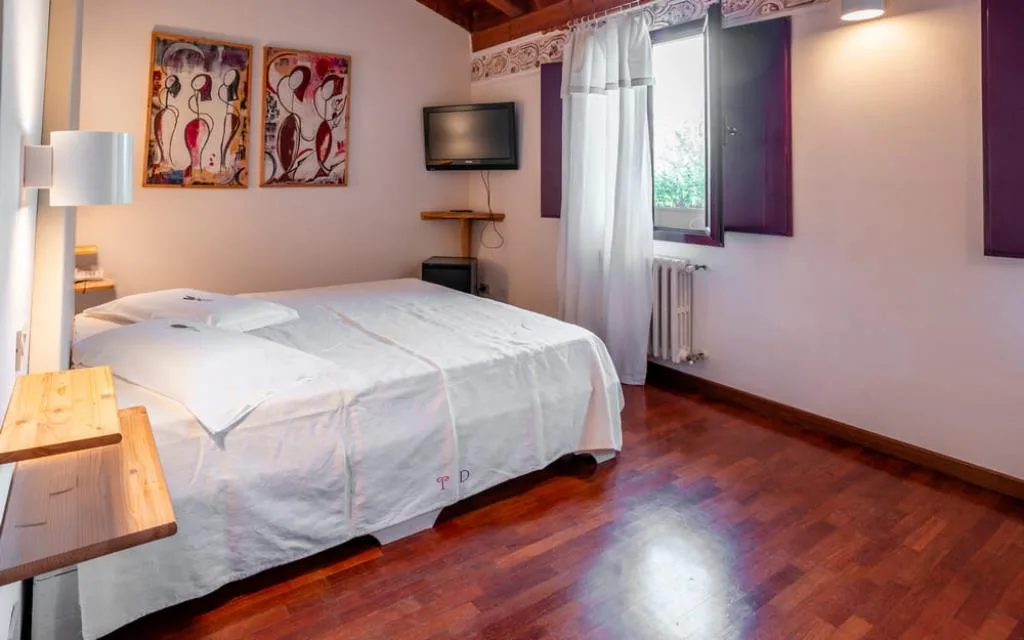Camera con letto matrimoniale, TV a parete, parquet e finestra con persiane viola