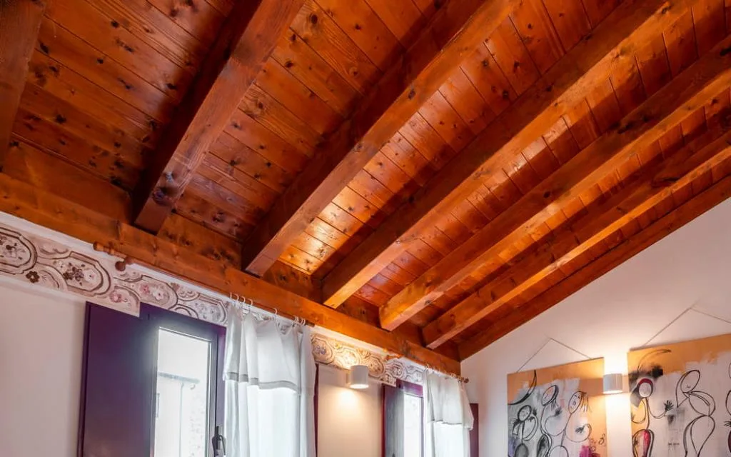 Soffitto in travi di legno con decori floreali e finestre con tende bianche