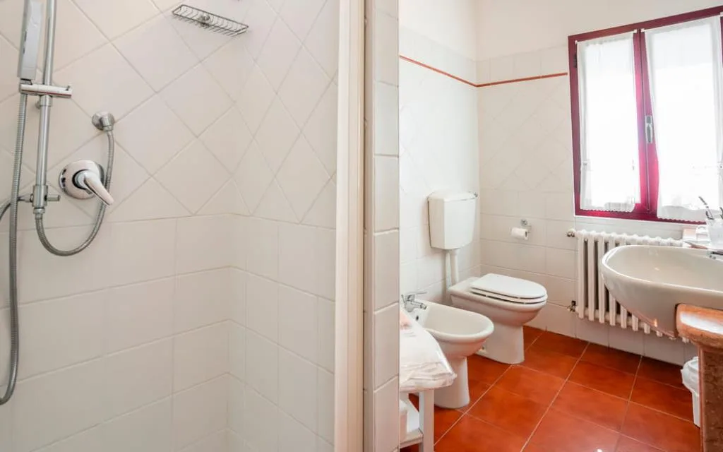 Bagno con doccia a muro, WC, bidet e finestra con cornice bordeaux