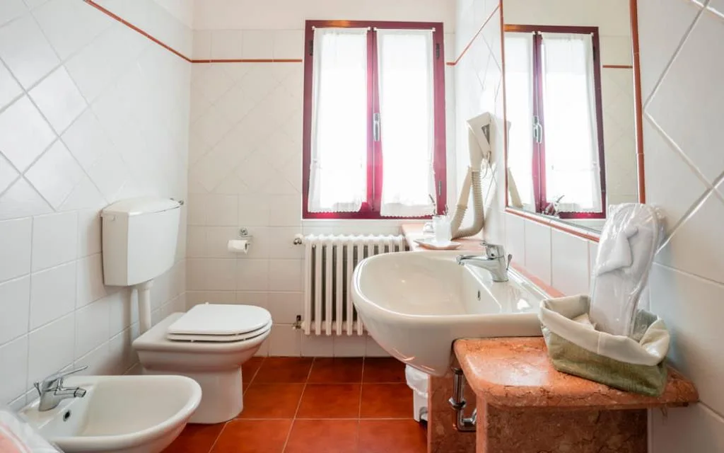 Bagno con WC, bidet, lavabo su piano in marmo rosa e finestra con tende bianche