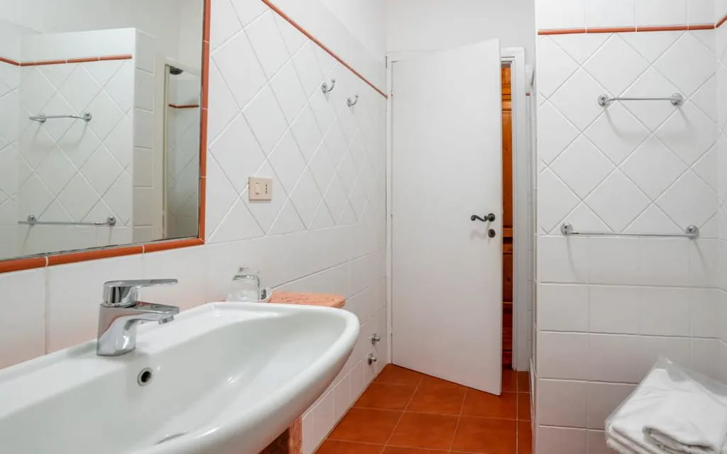 Bagno bianco con lavabo, specchio e porta aperta su ambiente in legno