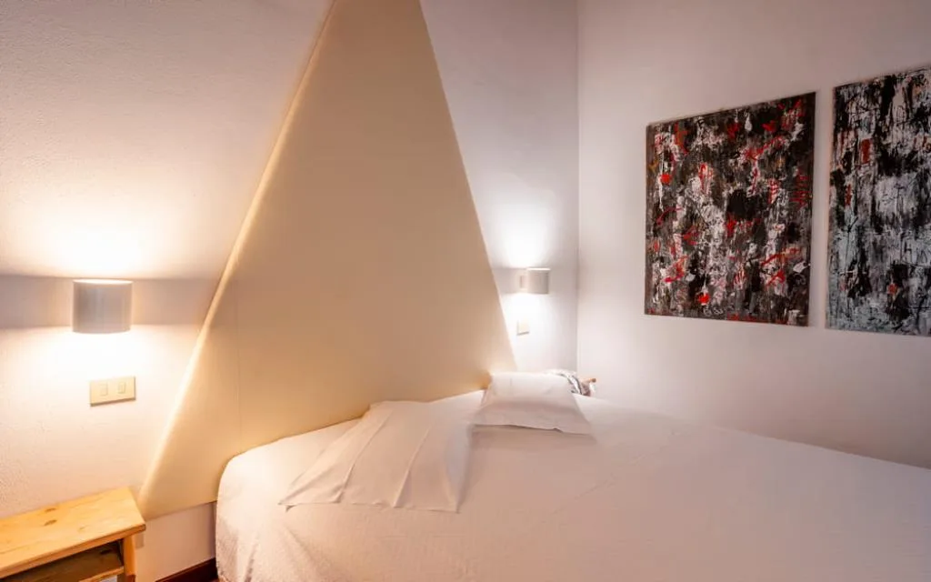 Camera con letto, parete triangolare bianca, applique e dipinti astratti