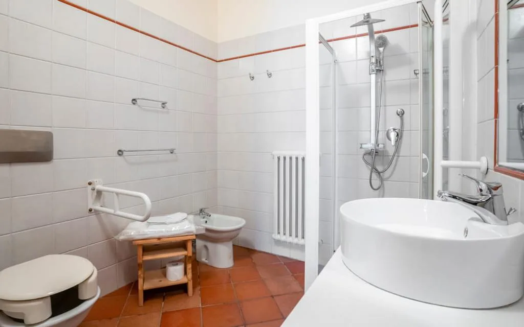 Bagno accessibile con maniglioni, WC, bidet, doccia e lavabo su pavimento in cotto