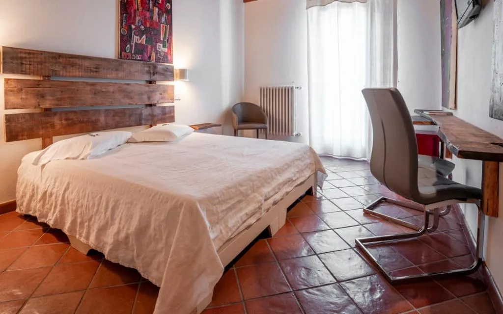 Camera con letto matrimoniale, testiera in legno, scrivania e pavimento in cotto