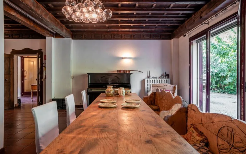 Sala da pranzo con tavolo in legno, pianoforte e porta vetrata sul giardino