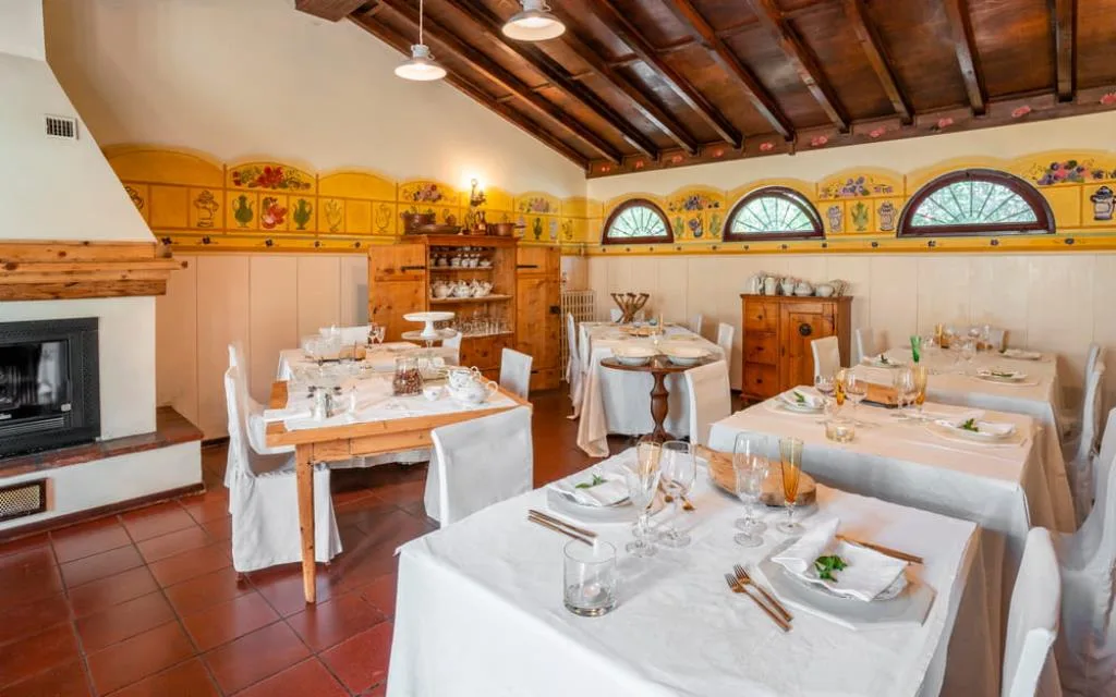 Sala ristorante con soffitto in legno, camino e tavoli apparecchiati con decori gialli