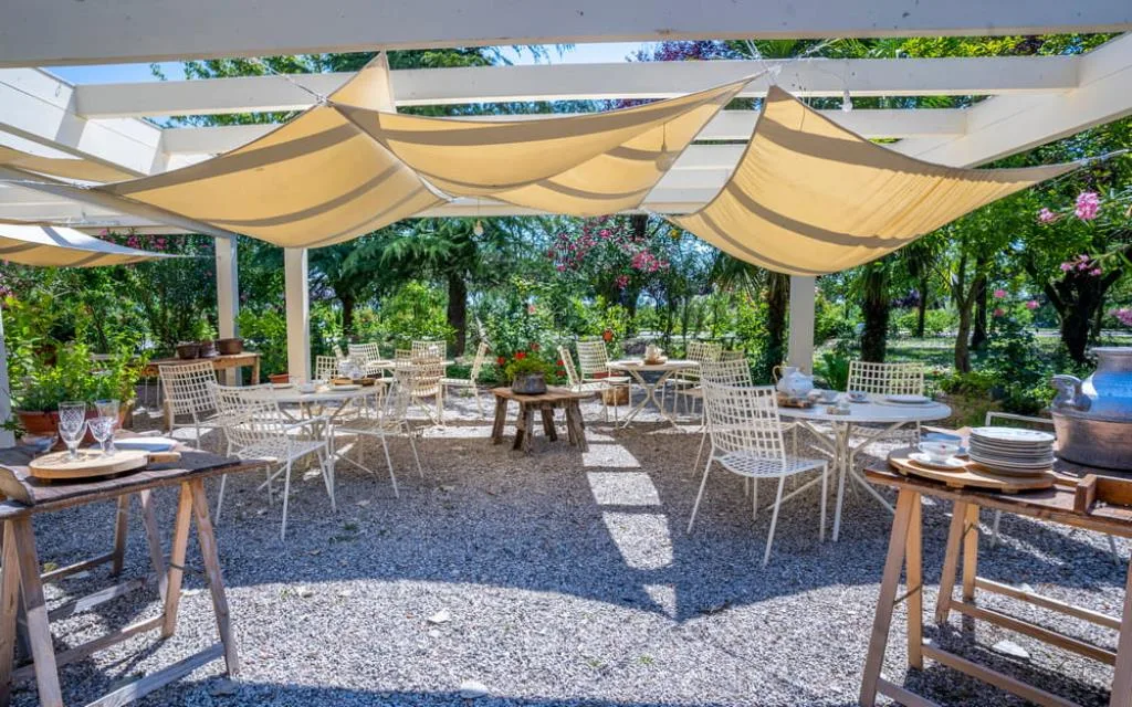 Area esterna con pergolato, tende ombreggianti, tavoli e sedie in ferro nel giardino