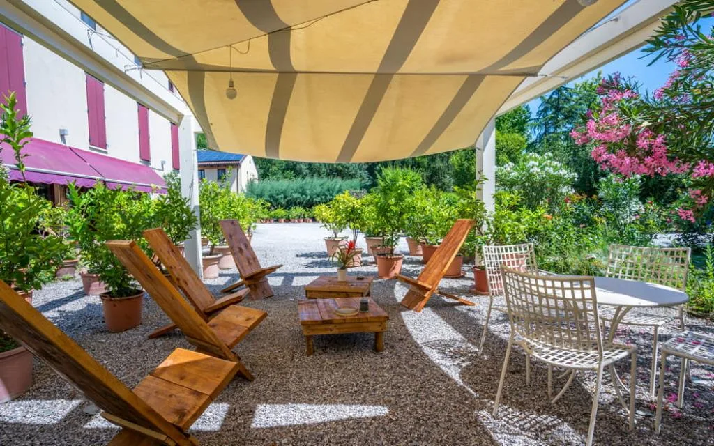 Terrazza con pergolato, sedie in legno, tavolini e vegetazione fiorita