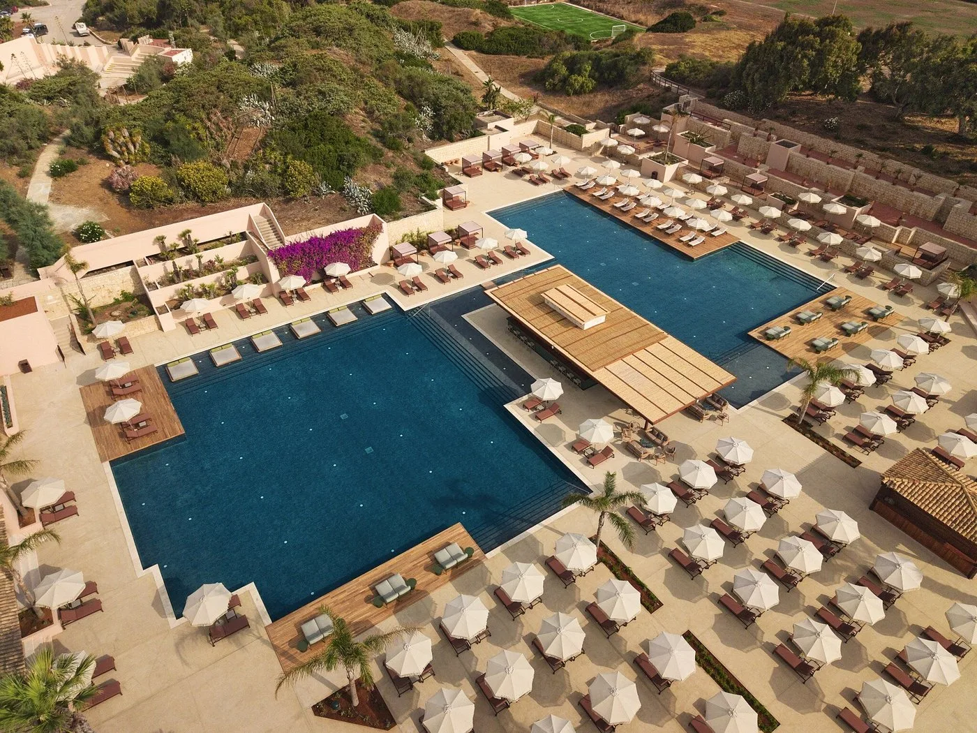 Veduta aerea di ampia piscina geometrica con numerosi lettini e ombrelloni bianchi