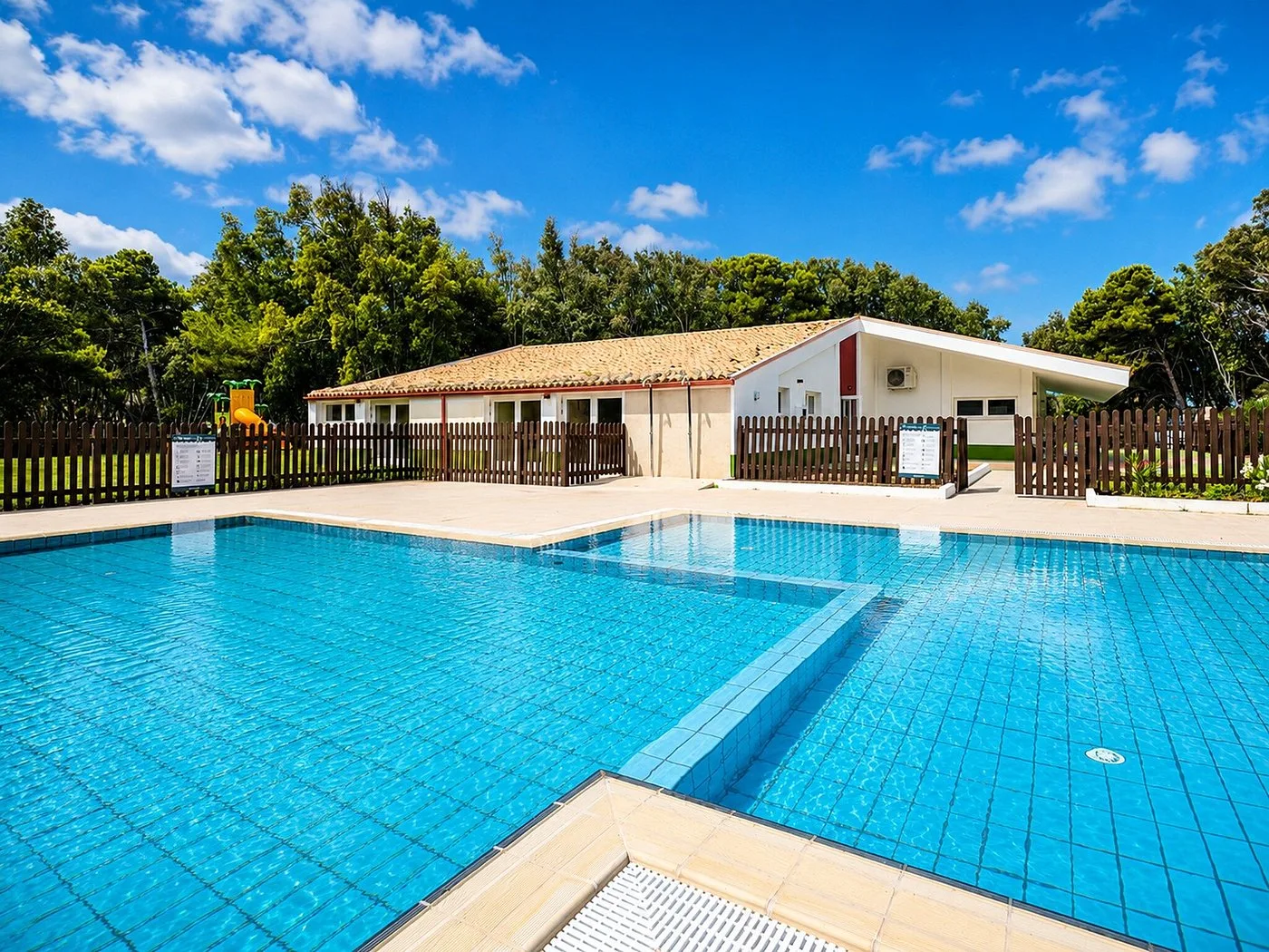 Piscina per bambini con area giochi recintata e cielo azzurro