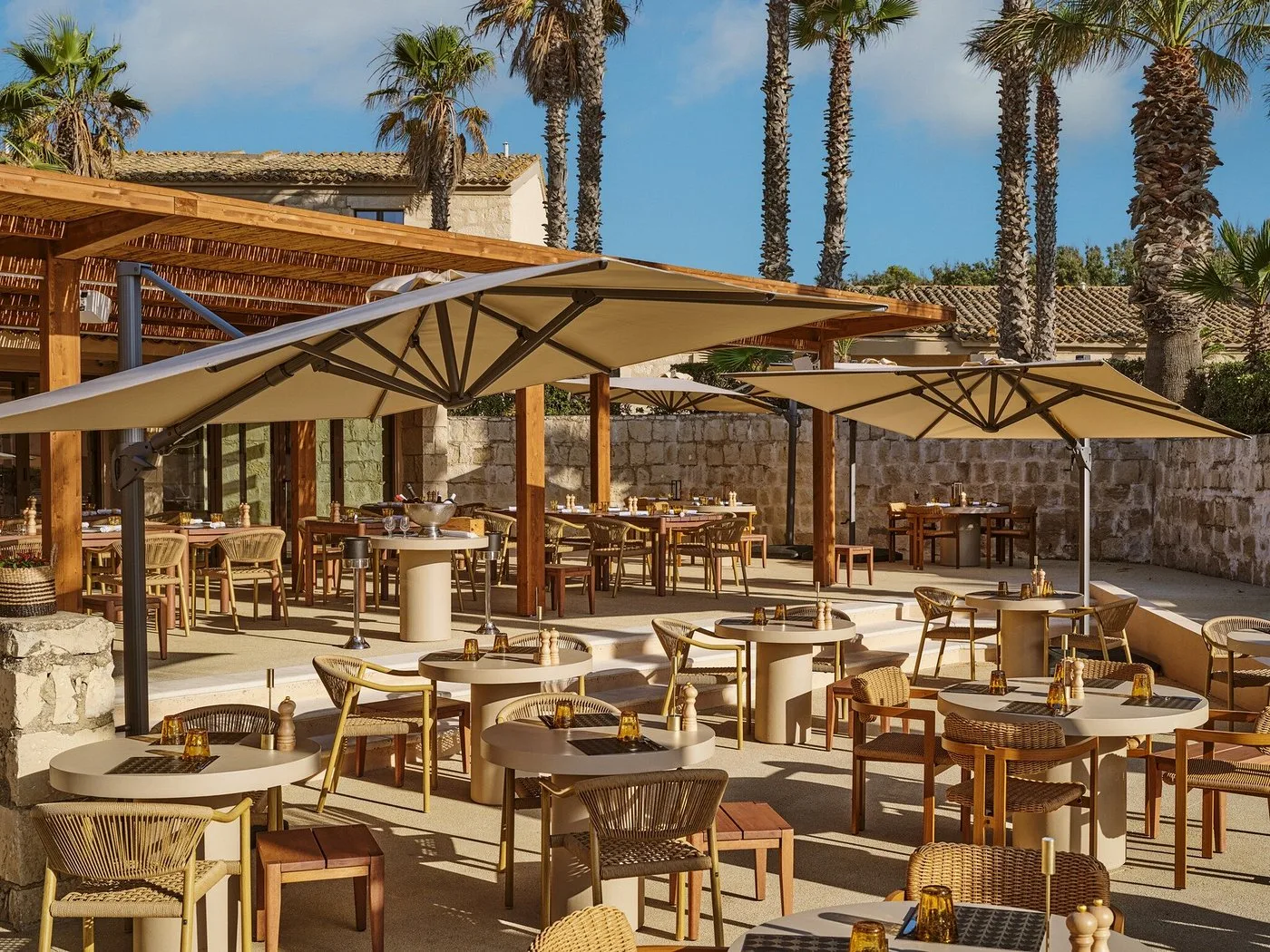 Terrazza del ristorante all'aperto con tavoli, sedie in rattan e grandi ombrelloni tra le palme