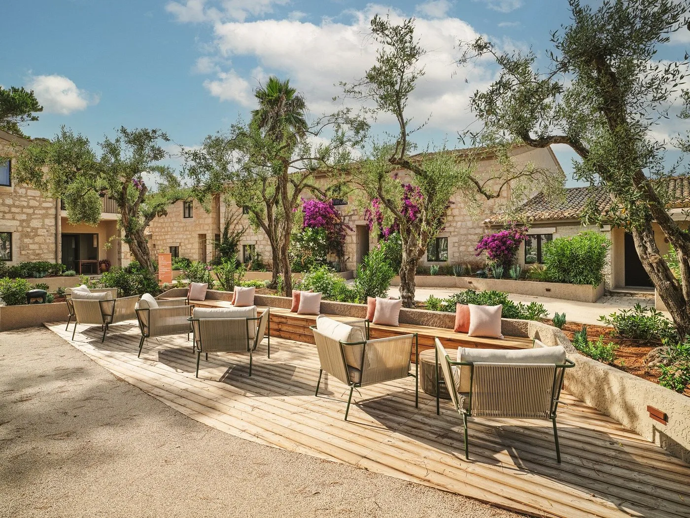 Area lounge esterna con poltrone e divani tra ulivi e bougainvillea presso edifici in pietra