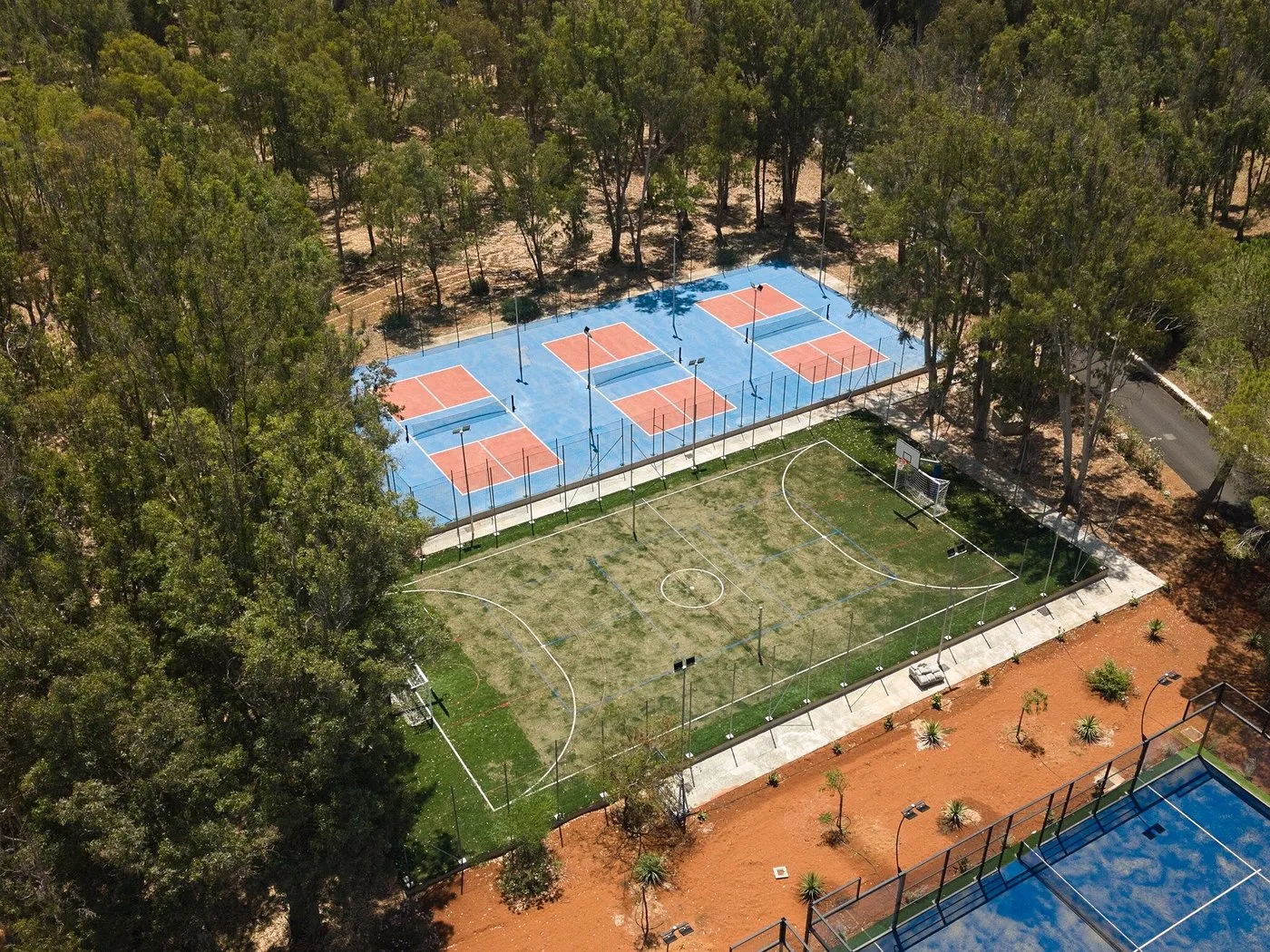 Veduta aerea di campi sportivi da tennis e calcio immersi nella pineta