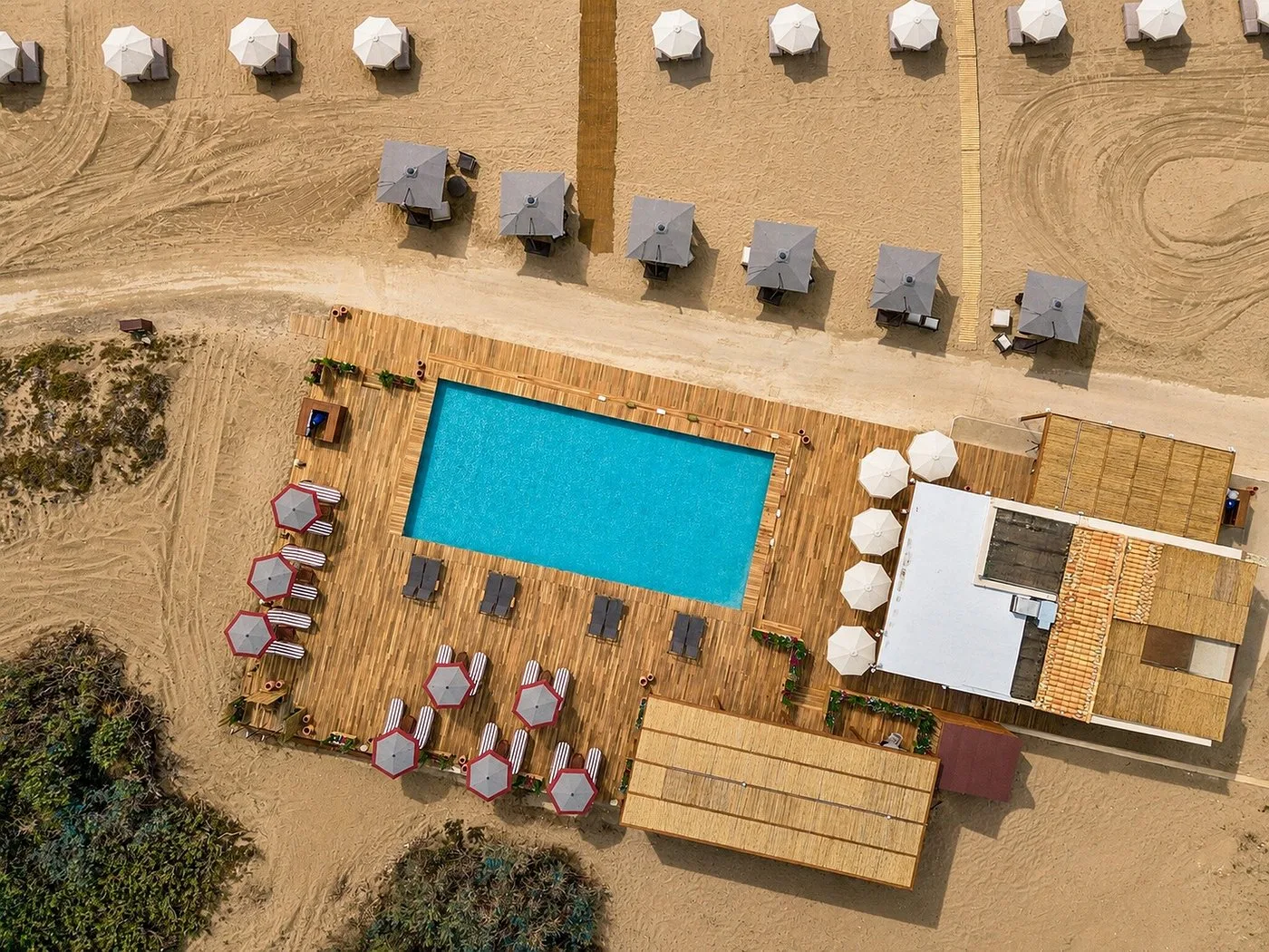 Vista aerea di piscina sulla spiaggia con pedana in legno, ombrelloni e lettini